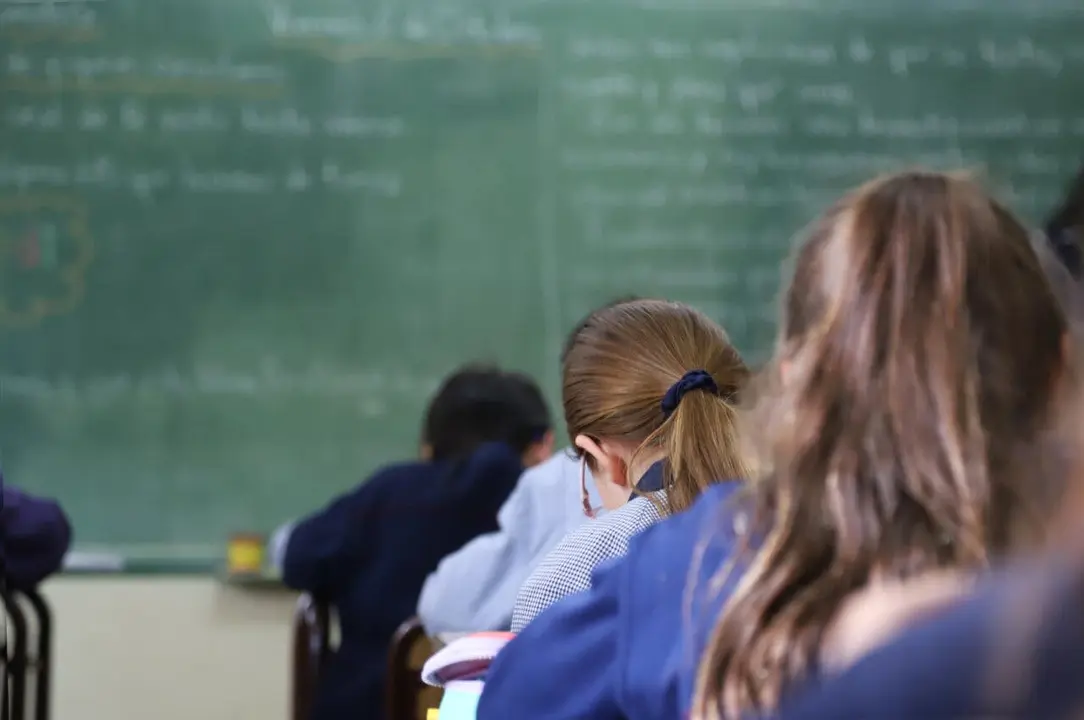 Students in class copying text from the blackboard. Classroom with green blackboard in the background and students. Primary school with children and children studying. Background with copy space.