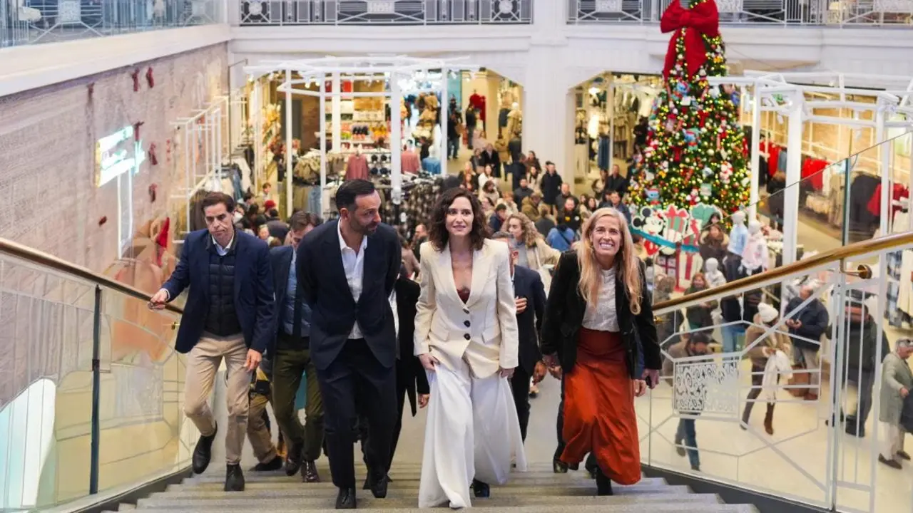 Un grupo de personas sube las escaleras en un centro comercial decorado para las fiestas. La atm&oacute;sfera es festiva y animada.