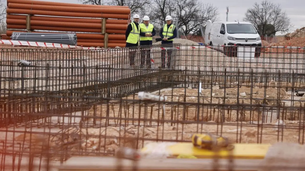 Tres trabajadores revisan los planos en un sitio de construcci&oacute;n. Se observan materiales apilados y estructuras de acero.