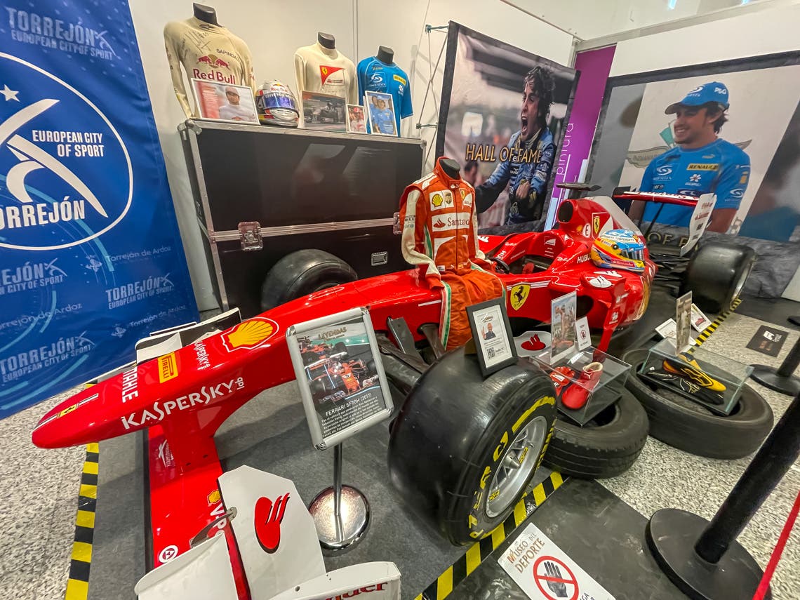 Exposición de Fórmula 1 en Torrejón de Ardoz con Ferrari y trajes de pilotos.